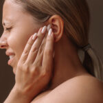 Profile of a young caucasian blonde woman holding her ears with her hands. Ear otitis